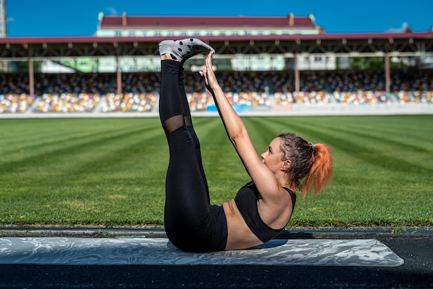 녹색 경기장 배경에서 요가나 필라테스 운동을 하는 여성 트레이너. 활동적인 라이프스타일, 건강한