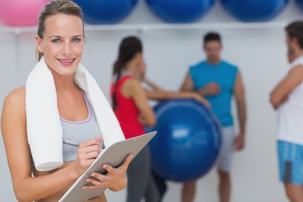 Female trainer holding clipboard with fitness class in background