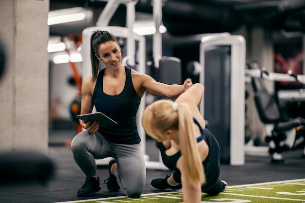 A female trainer is helping sportswoman with workouts in a gym