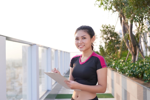 公園に立っているときにクリップボードに書く女性トレーナー。