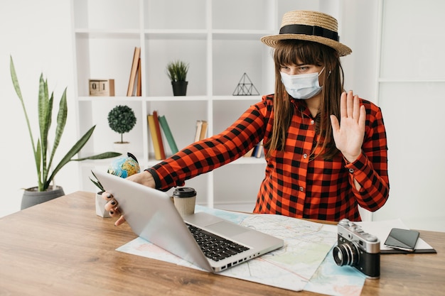 Foto blogger di viaggio femminile con maschera medica in streaming con il laptop a casa