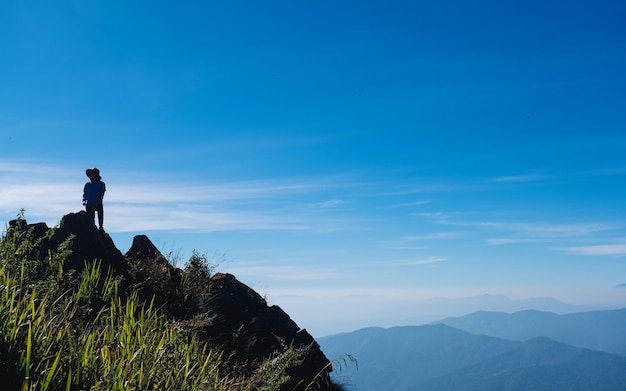 Un viaggiatore femminile che fa un'escursione e che si siede sulla cima della montagna che esamina una bella vista