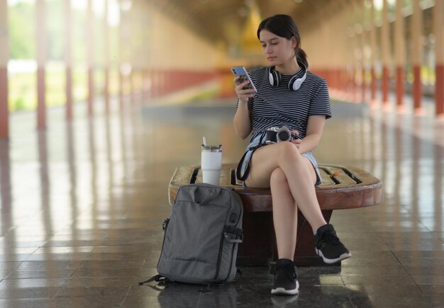 写真 プラットフォームで列車を待っている女性旅行者がスマートフォンを見ています