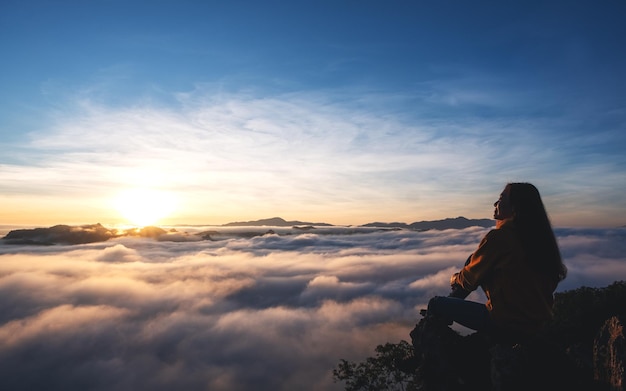 A female traveler sitting on the mountain peak watching sunrise and sea of fog