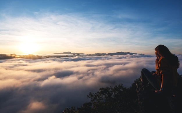 A female traveler sitting on the mountain peak watching sunrise and sea of fog