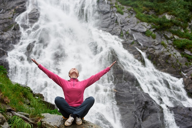 Female traveler sitting on waterfall Balea in Romania