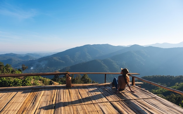 Una viaggiatrice seduta sul balcone di legno e guardando una bellissima vista sulle montagne