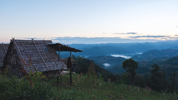 A female traveler sitting in wooden cabin looking at a beautiful mountain and nature view before sunrise