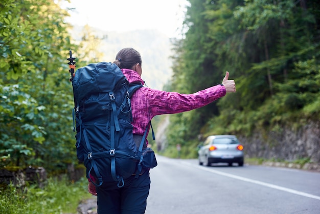 写真 バックパックを持つ女性旅行者が道路で車をキャッチしています。