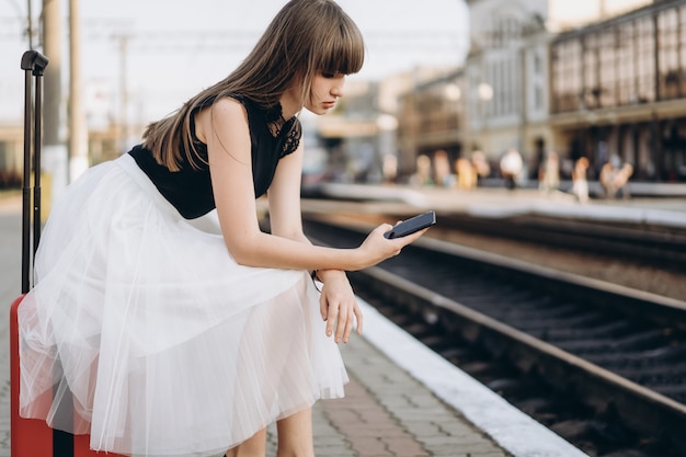 Female traveler with red suitcase waiting train on railway station