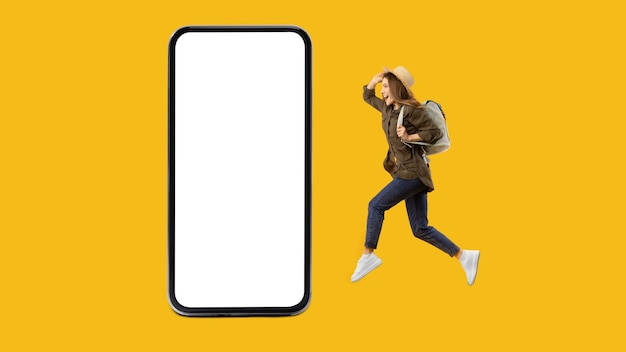 Female traveler woman jumping near huge smartphone on yellow background