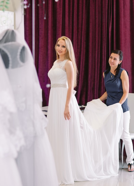 Female trying on wedding dress in a shop with women assistant.