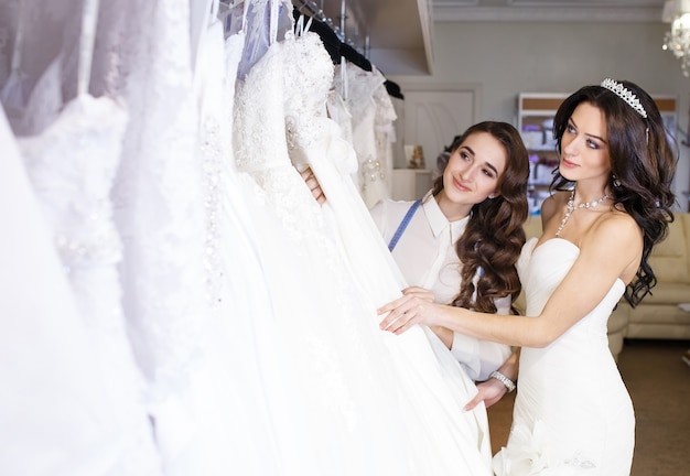 Female trying on wedding dress in a shop with women assistant.