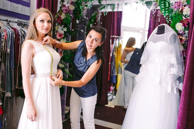 Photo female trying on wedding dress in a shop with women assistant.