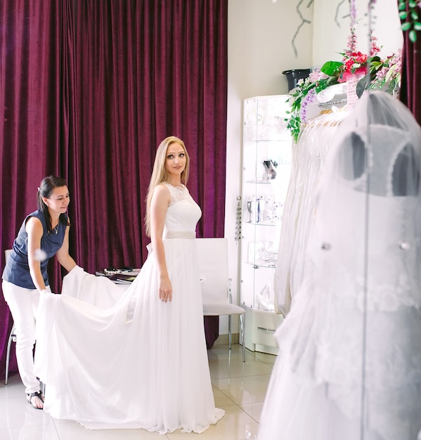 Prova femminile sul vestito da sposa in un negozio con l'assistente delle donne.