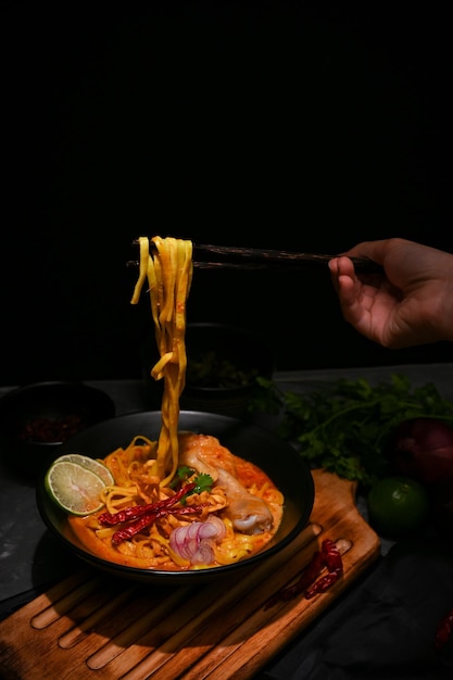 Una femmina che usa le bacchette per mangiare i suoi khao soi kai o gli spaghetti al curry della thailandia settentrionale