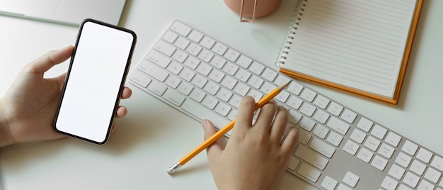 Female using mock up smartphone while typing on computer keyboard on white table