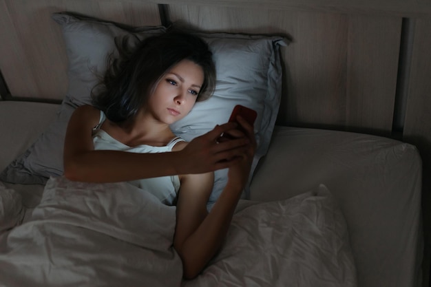 Female using smartphone in bed at night. Smartphone and social networks dependence. Insomia and harm of smartphone before going to bed.