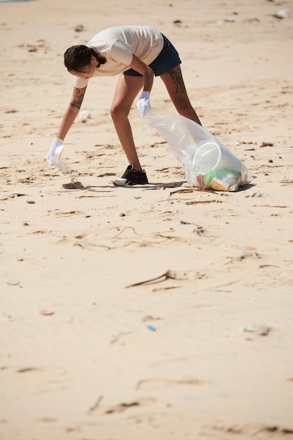 Female volunteer cleaning up plastic wastes on sandy ocean coast