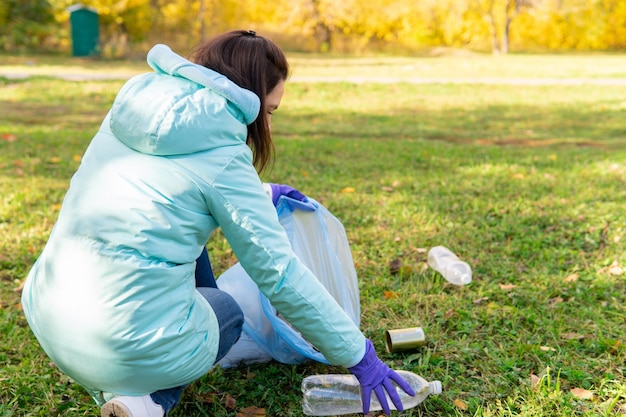 Photo a female volunteer cleans plastic garbage in nature it is located on the river bank with a waste bag she holds a plastic bottle