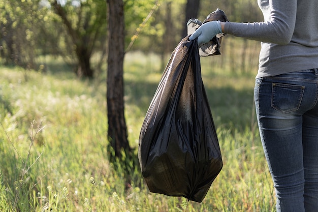 Female volunteer collects trash in the forest. Environmental pollution concept.