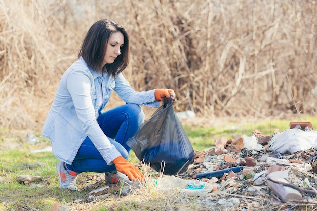 Female volunteer holds a bag with collected plastic cleaning the forest and park from garbage