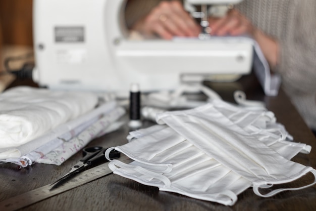 Female volunteer sews protective antivirus masks on a sewing machine at home