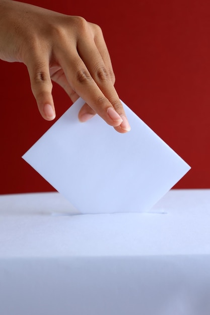 Photo female voter put vote card to ballot box with red background