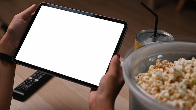 Female watching online movie on digital tablet and eating popcorn in living room