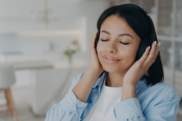 Female wearing wireless headphones listening to relaxing music\
or meditation enjoying sound at home