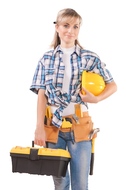 Female wearing working clothes with toolbelt holding hardhat and toolbox isolated on white