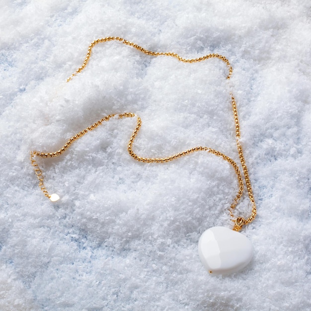 Female white heart shaped agate pendant with golden chain on white snow background. Close-up shot