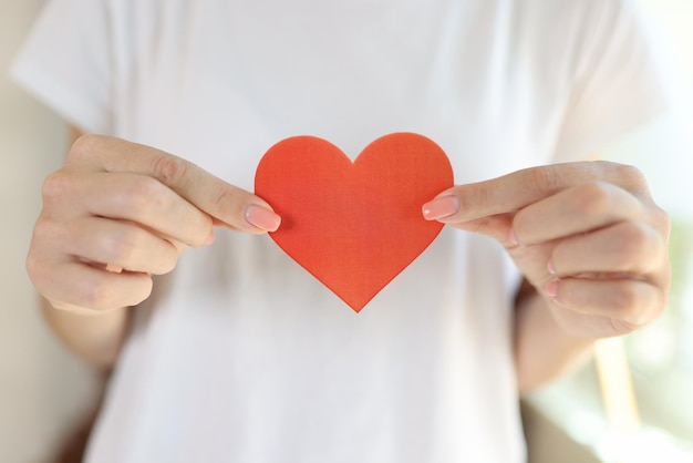 Photo female in white tshirt holds red heart in her hands in front of her body