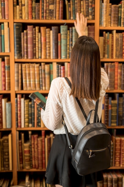 Femmina con lo zaino che sceglie il libro in biblioteca