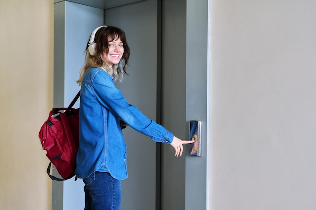 Female with backpack standing near elevator door pressing call button