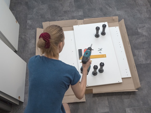 Female with a cordless driver collects furniture.