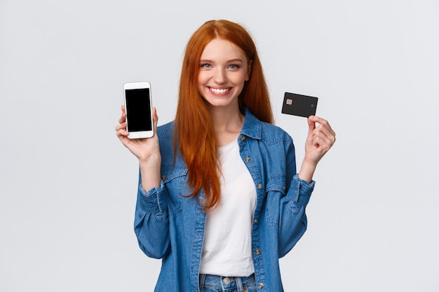 Фото Женщина с рыжими длинными волосами держит кредитную карту и показывая смартфон
