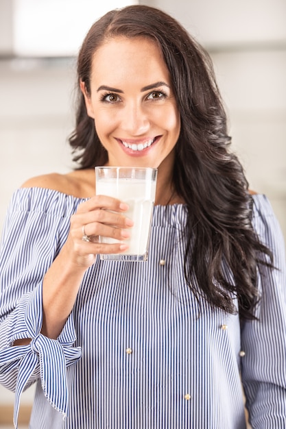 La donna con i denti bianchi sorride mentre tiene in mano un bicchiere di latte.