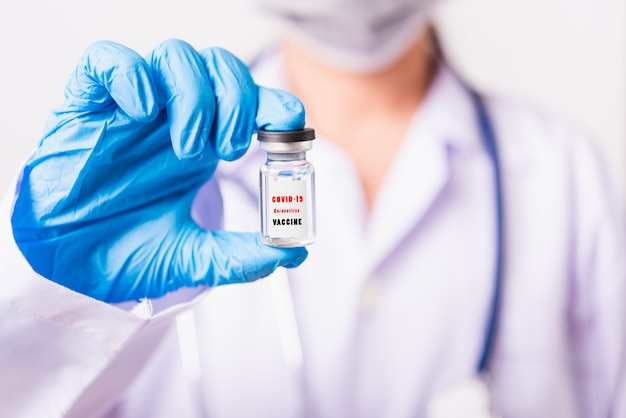 Female woman doctor in uniform wearing face mask protective in lab use finger hold vial vaccine bottle