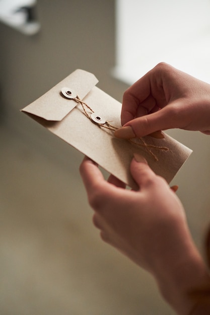 A female woman hand hold open a envelope and post card on the wood desk, top view 