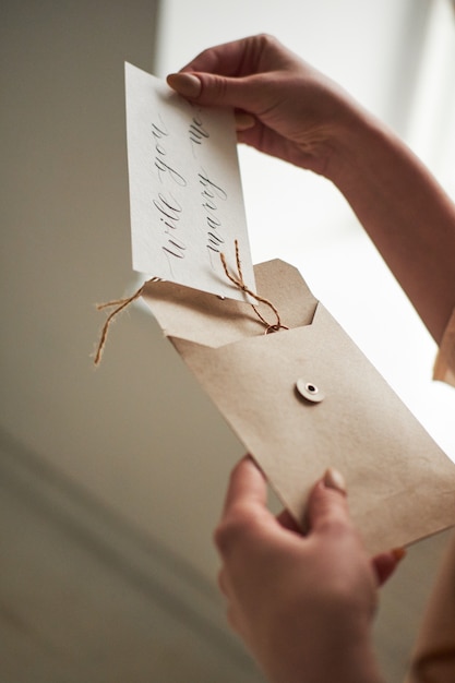 A female woman hand hold open a envelope and post card on the wood desk, top view