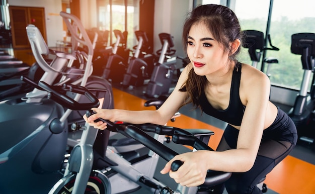 Female woman lifestyle using equipment machine exercise bike for training cardio workout at fitness gym