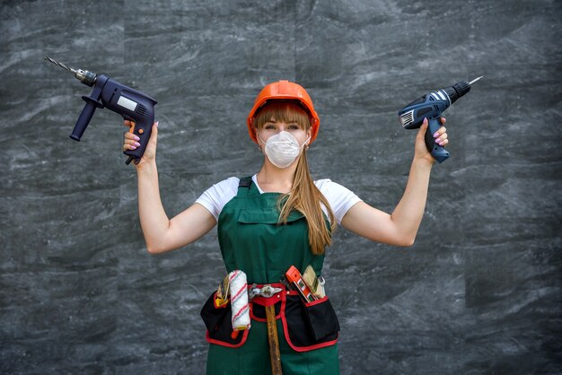 Female worker holds drill in hand on grey background. Concept of building, repair, renovation.