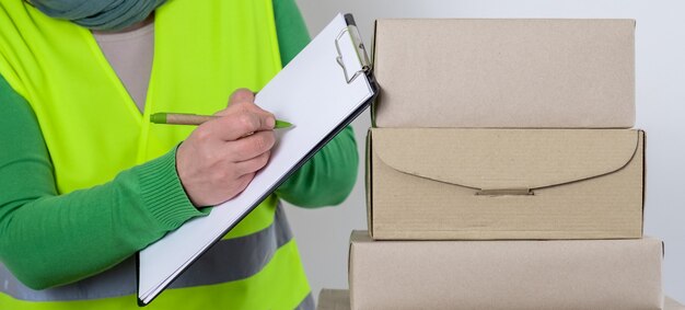 Foto la lavoratrice è in una maglia verde in piedi vicino a molte scatole di carta con ordine vuoto, concetto di consegna.