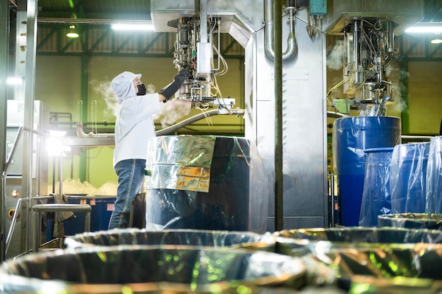 Lavoratrice in una fabbrica di ketchup riempitrice asettica automatica controllata che riempie il ketchup in grandi vasche in un impianto industriale nell'industria alimentare asiatica agroindustria