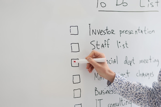 Photo female worker marks schedule points written on whiteboard in office woman makes to do list to