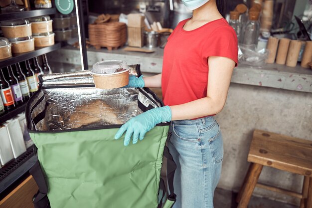 Female worker in protective face mask packing food indoors