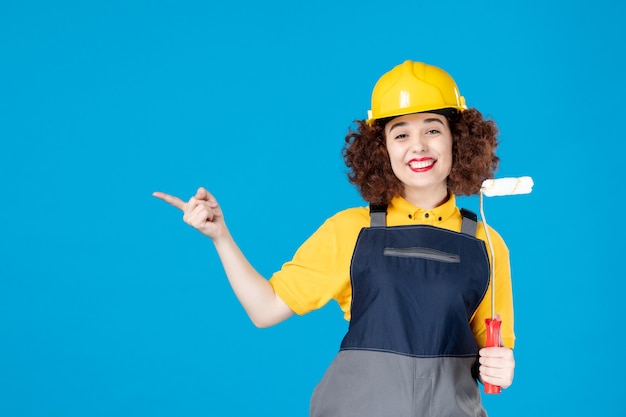 Lavoratrice in uniforme con rullo di vernice su un blu