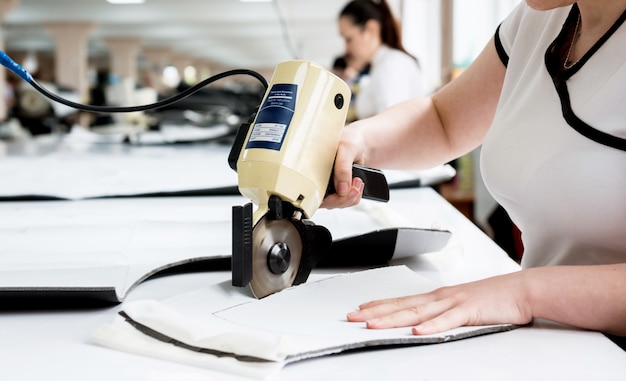 Female worker uses electric cutting fabric machine. Fabric industry production line.