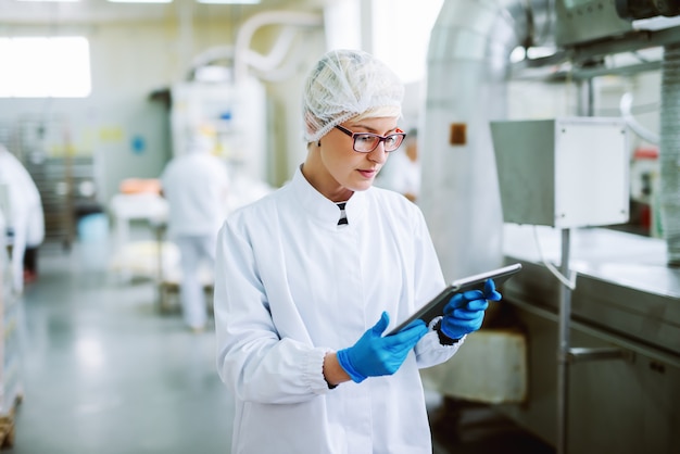 Женский работник используя таблетку для контролировать продукты пока стоящ в фабрике еды.